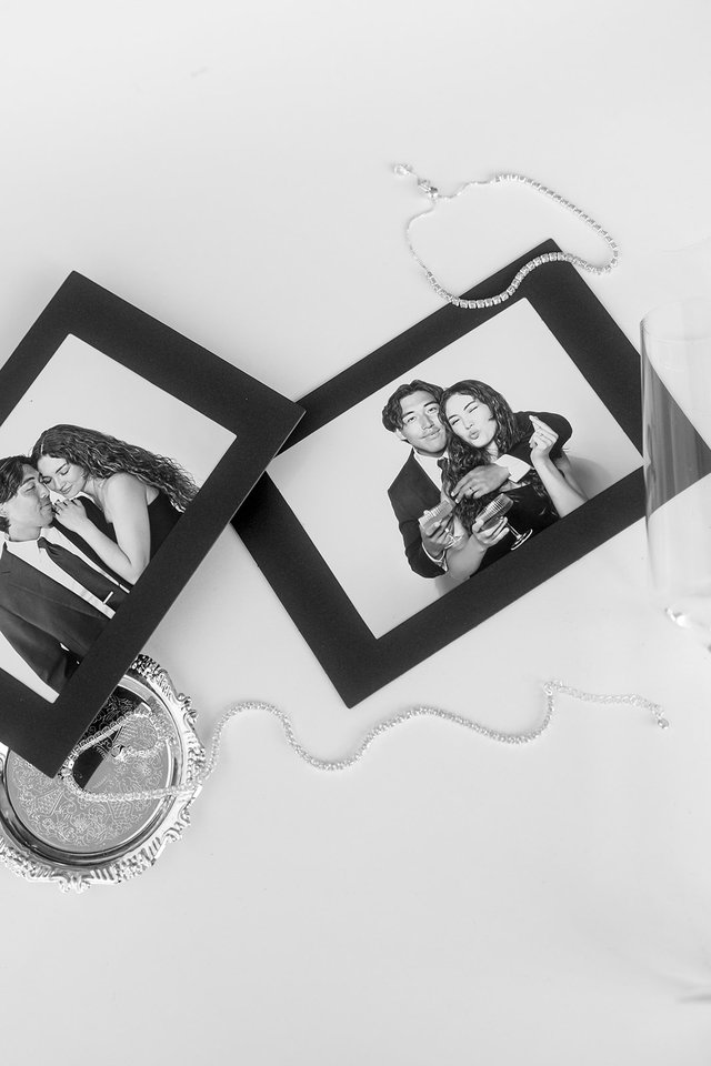 Black-and-white shot of two portrait prints on a tabletop with necklace and glass