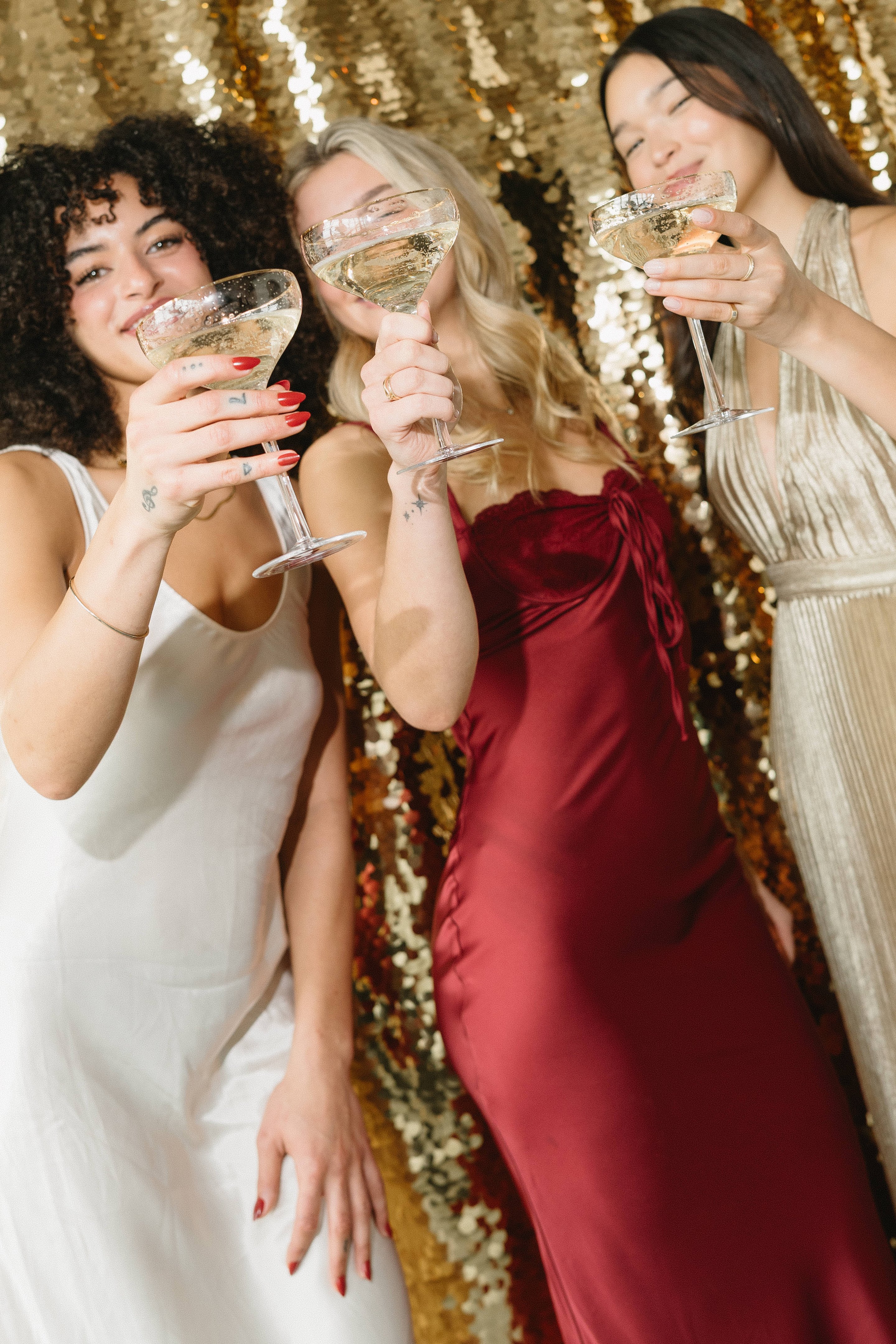 Three women raising coupe glasses at a gold sequin wall