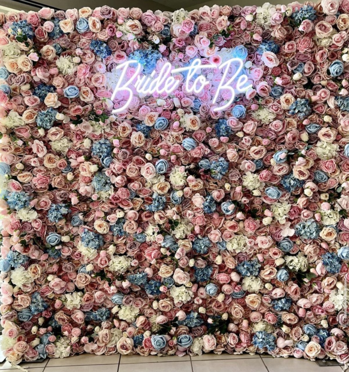 The Naomi flower wall: pink, blue and cream blooms, with a neon sign