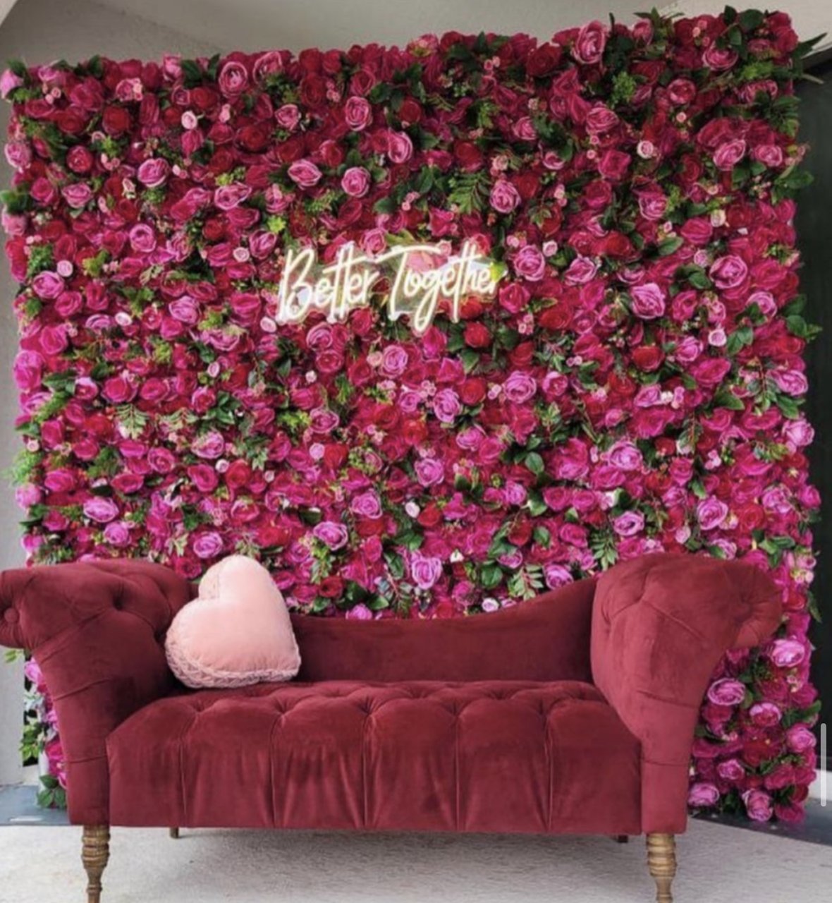 The Queen flower wall: deep pink and magenta roses, with a neon sign and a velvet settee