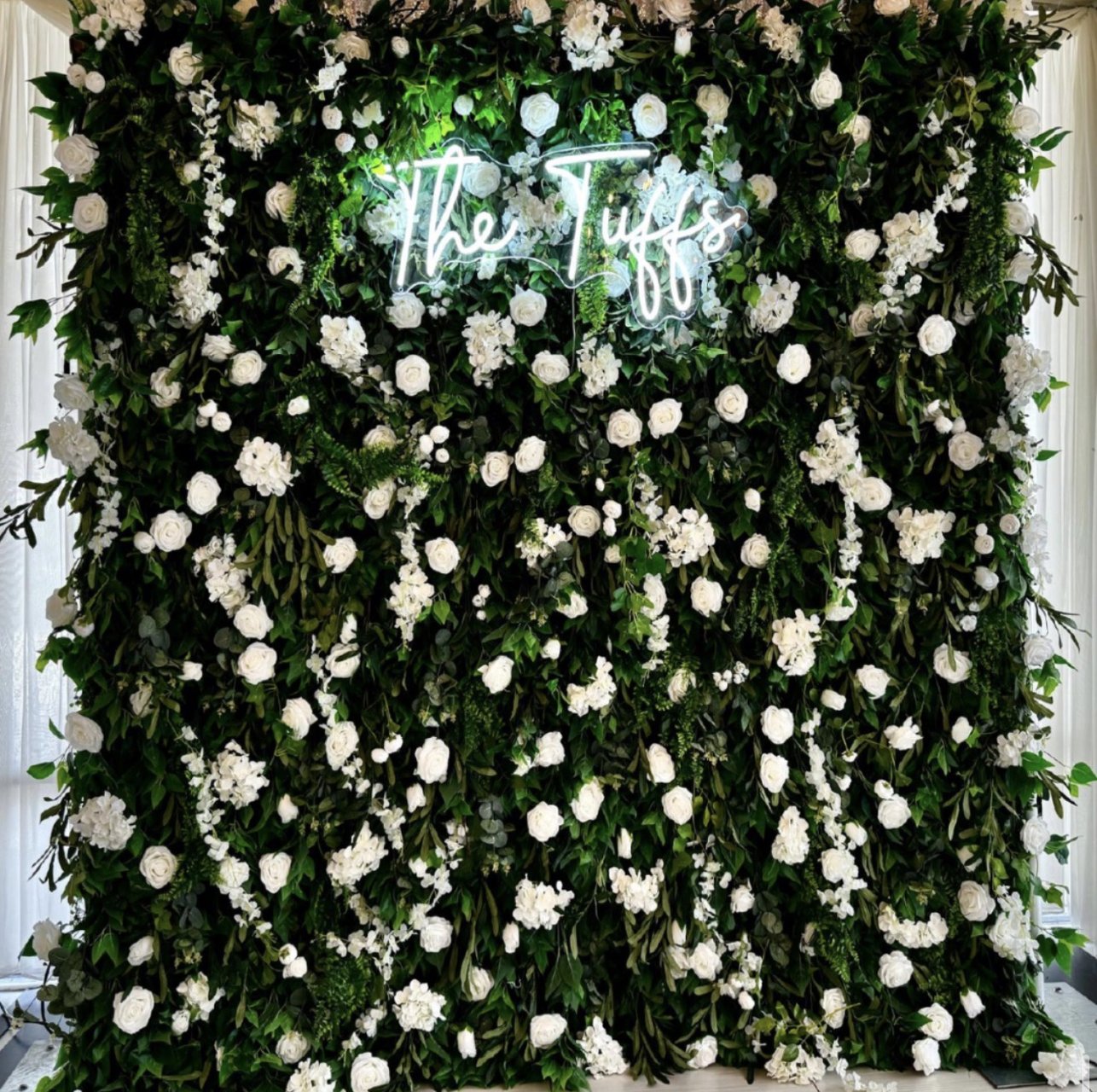 The Spring flower wall: white blooms on deep green foliage, with a neon sign